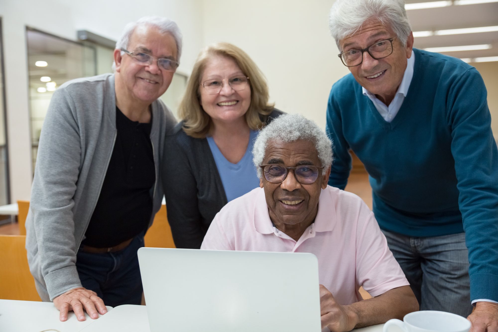 Four smiling older adults gathered around a laptop.